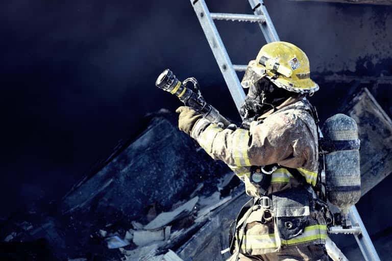 A firefighter in full gear fighting a fire with a hose, emphasizing courage and safety.