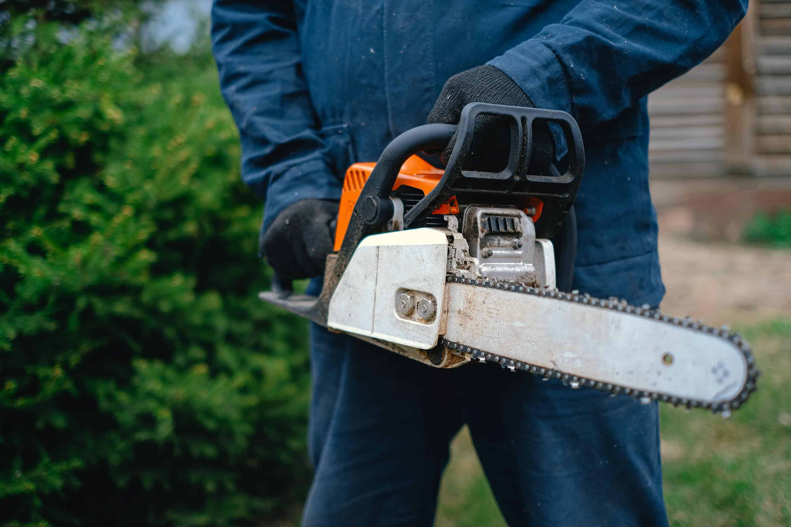 Close-up of a worker holding a chainsaw, ideal for carpentry and outdoor renovations, captured outdoors.