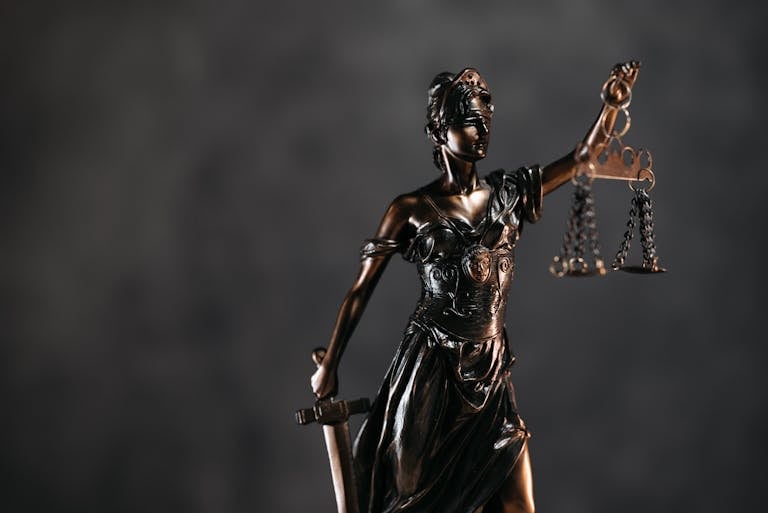 Detailed bronze Lady Justice statue with scales and sword against a dark background, symbolizing law and justice.