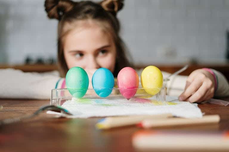 A child happily decorates colorful Easter eggs on a wooden table indoors.