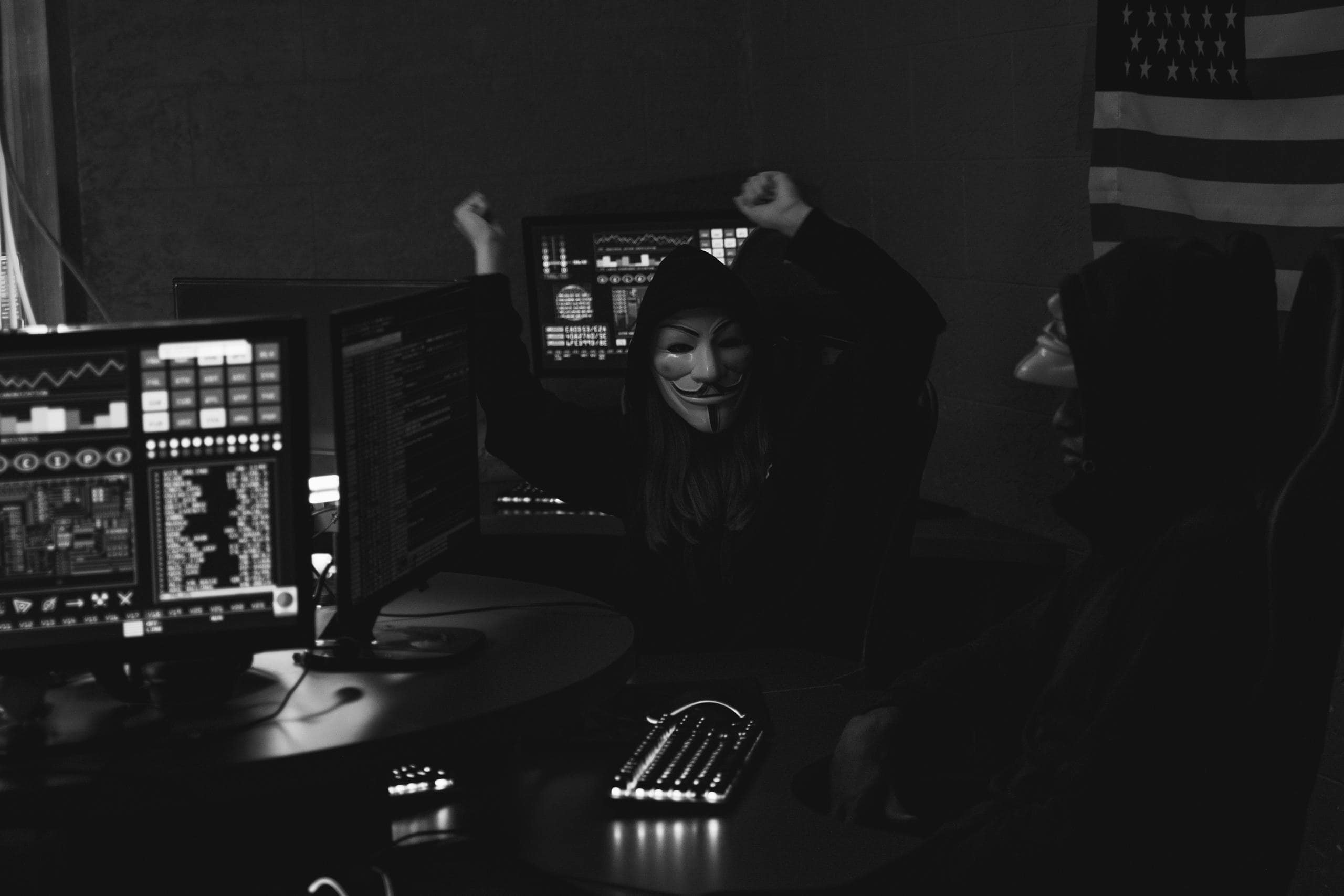 Hacker group with masks celebrating a successful cyber attack in a dimly lit room.