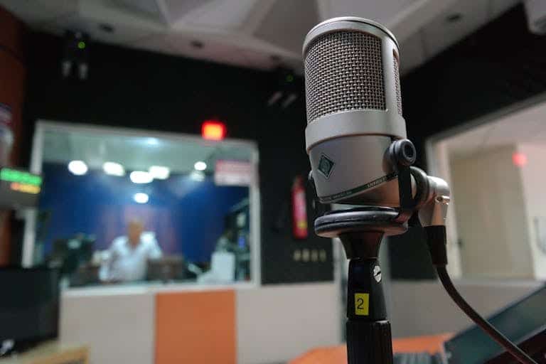 Close-up of a microphone in a recording studio with a blurred sound engineer in the background.