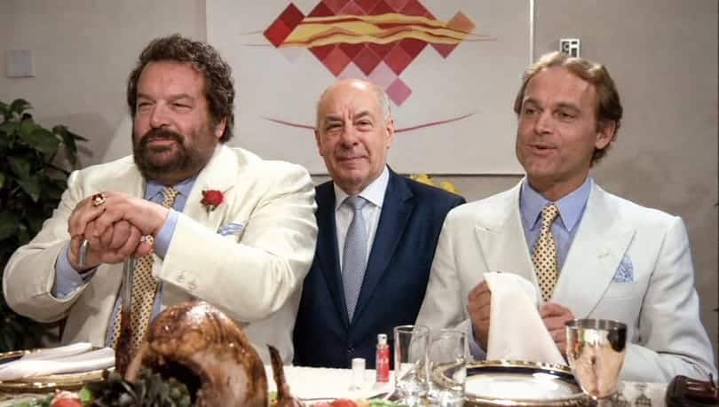 Egy három férfi ül egy étkezőasztalnál ünnepi vacsorán, elegáns öltözetben.